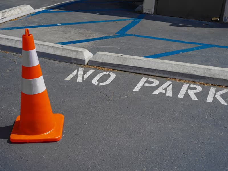 Orange traffic cone on a blue-marked parking area with ‘no park’ painted on the asphalt