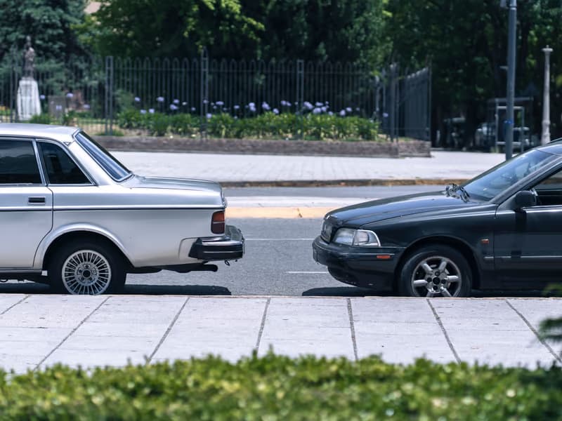 Two cars parked at the kerb in front of a hedge and fence
