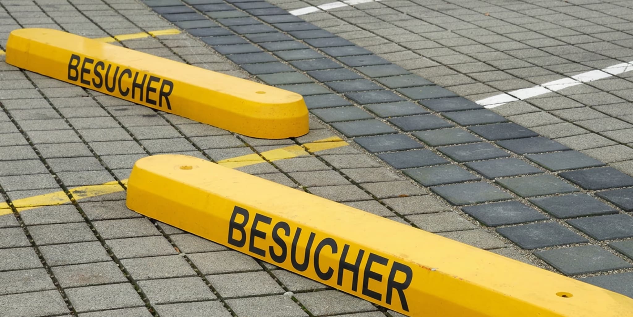 Two yellow parking blocks marked “BESUCHER” (visitor) on a paved car park