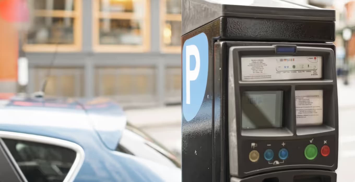 Black parking ticket machine with a blue P sign, a parked car blurred behind it