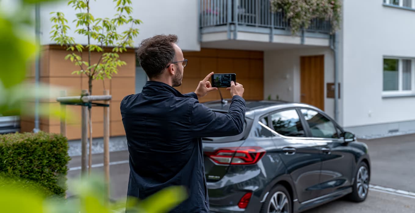 Man photographing a dark parked car with his smartphone in a residential courtyard